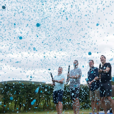 Group of men outside releasing blue confetti cannons