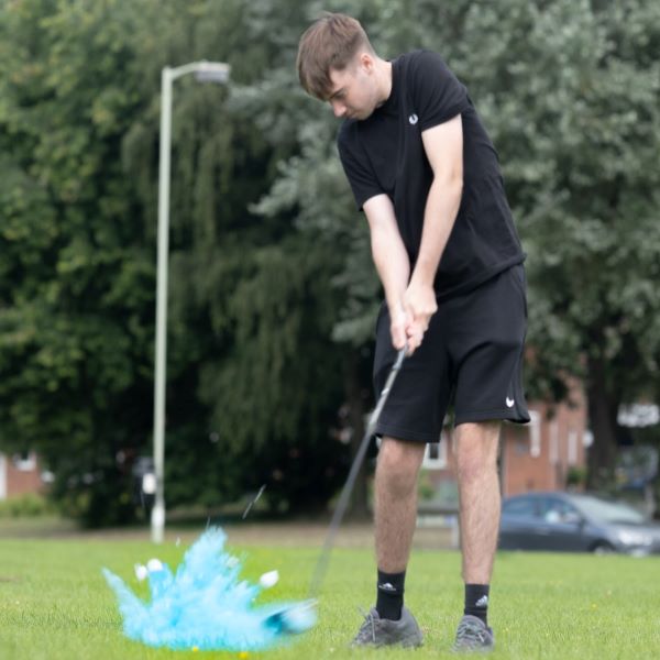 Young man hitting a blue powder exploding golf ball