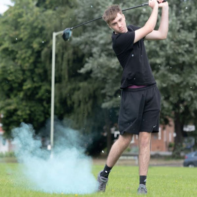 Young man with golf club above his head and blue powder in the air
