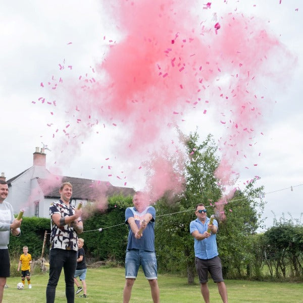 Group of men outside releasing pink powder and confetti cannons