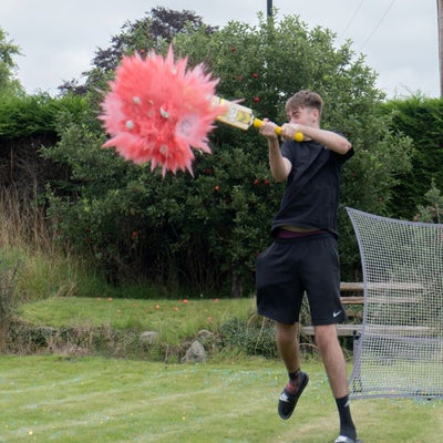 young man hitting a ball with cricket bat and pink powder exploding
