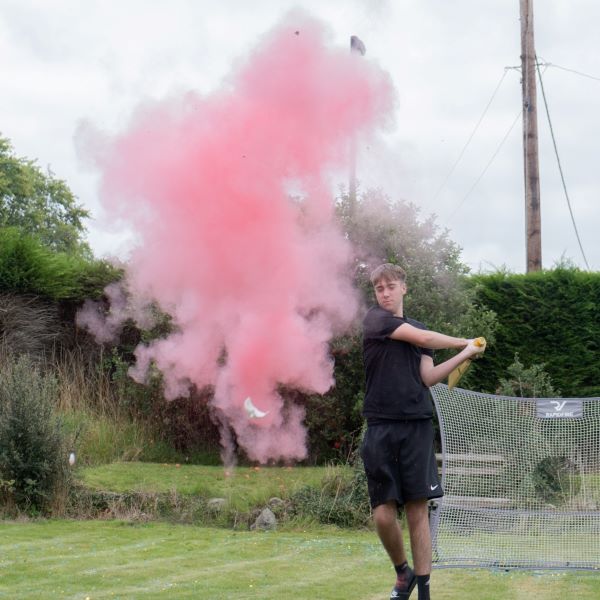 large pink plume in the air and a boy with a cricket bat