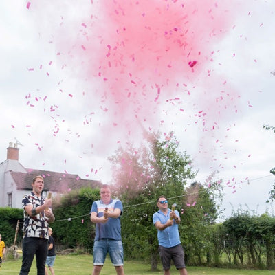 Three men outside releasing pink confetti & powder cannons